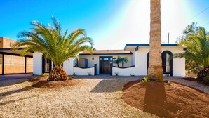 Una casa moderna de dos pisos con fachada blanca, puerta principal oscura y entrada de grava con palmeras.