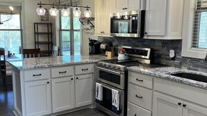 Una cucina moderna con mobili bianchi, un piano di lavoro in granito, elettrodomestici in acciaio inossidabile e un soffitto in legno.