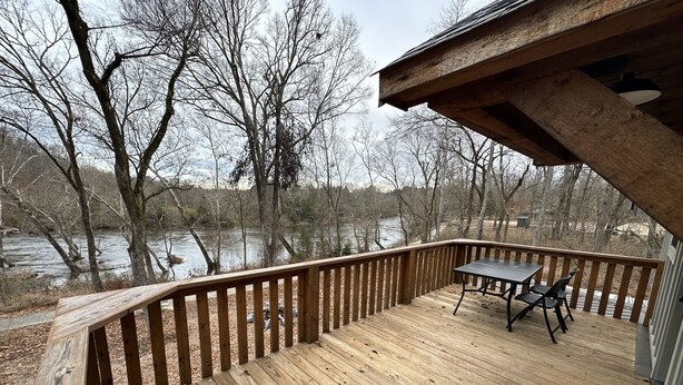Un pontile in legno con tavolo e sedie, affacciato su un fiume e alberi.