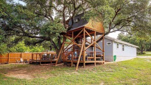 Une cabane dans les arbres avec une terrasse en bois et une petite maison en arrière-plan.