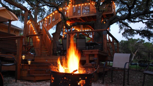 Une cabane dans les arbres avec un foyer et un espace salon extérieur.