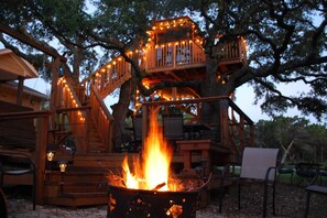 Une cabane dans les arbres avec un foyer et un espace salon extérieur.