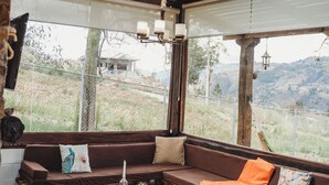 A cozy, rustic interior with a wooden bench seating area, a small table, and large windows offering a view of the outdoors. - Villa Nathalie -Cheerful Rustic House (Chican, Paute)