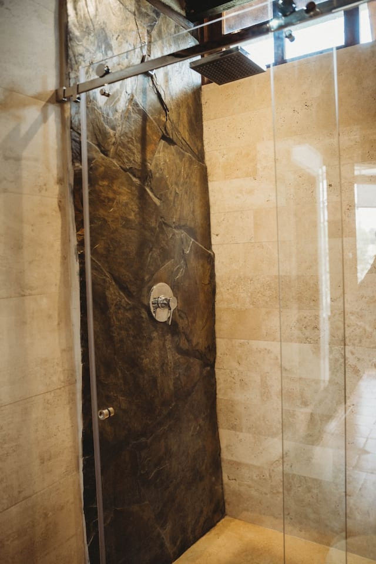 A shower with a marble wall and a glass door.