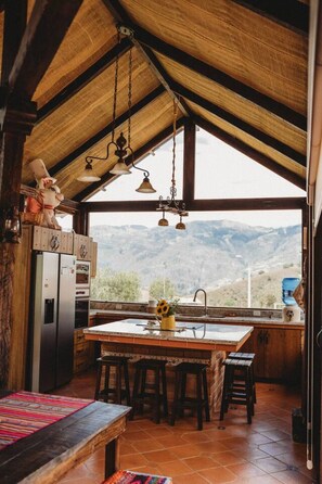 Una cucina rustica con un'isola grande, sgabelli di legno e vista sulle montagne.