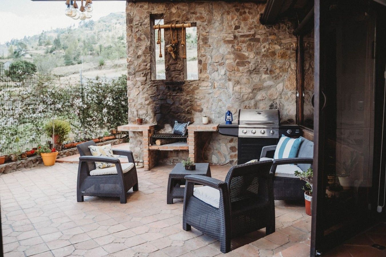 Eine Terrasse im Freien mit Steinmauern, einem Grill, Korbmöbeln und Blumentöpfen.