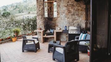 Eine Terrasse im Freien mit Steinmauern, einem Grill, Korbmöbeln und Blumentöpfen.