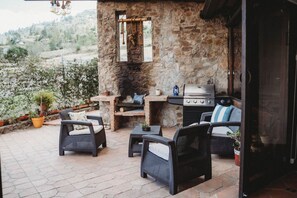 An outdoor patio with stone walls, a grill, wicker furniture, and potted plants. - Villa Nathalie, jaccuzzi, king size bed+hammock (Chican, Paute)