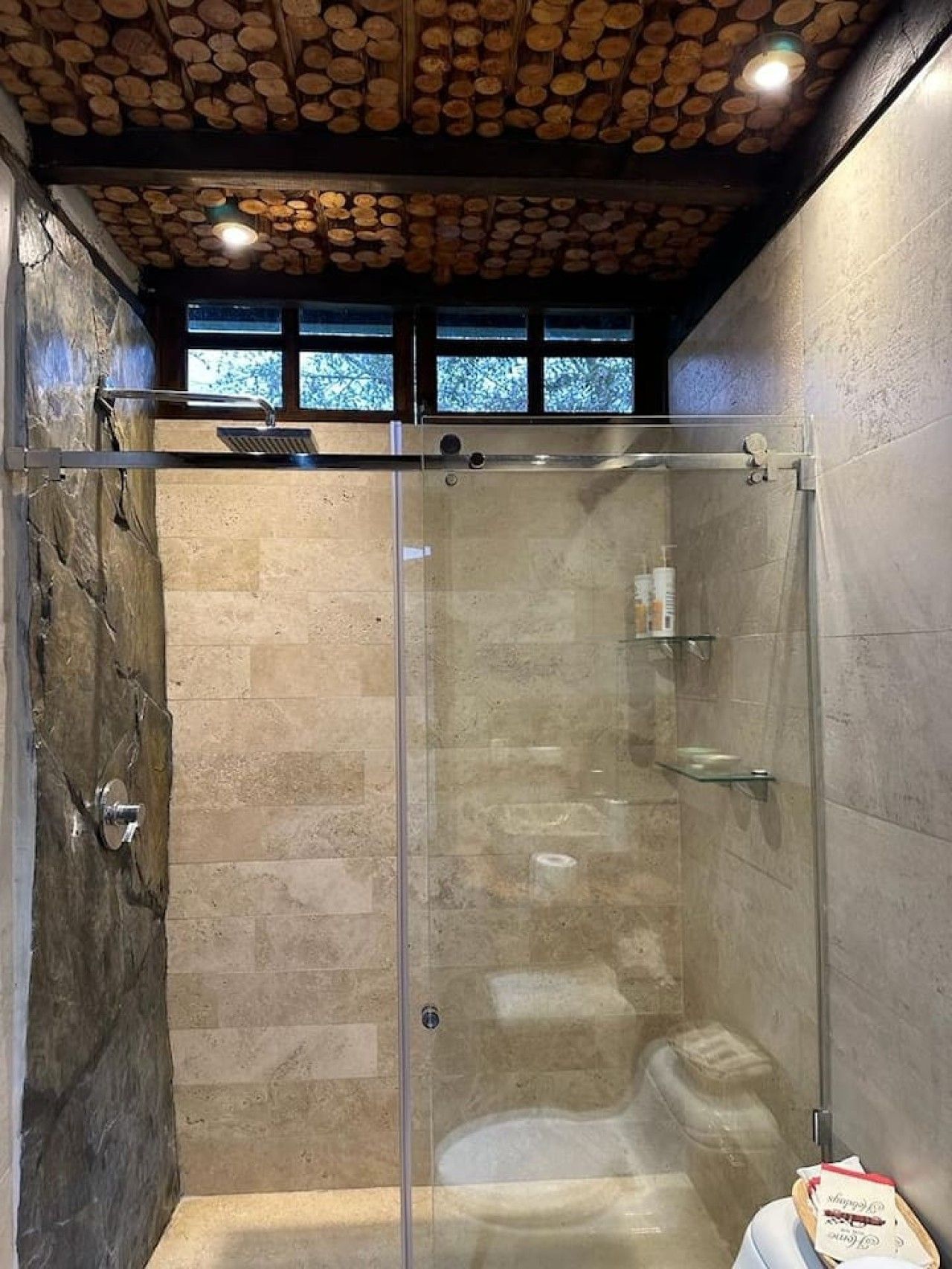 A glass-enclosed shower with stone walls and a wooden ceiling.