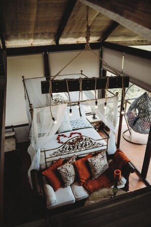 Ein Bett mit Baldachin, ein Hängesessel und ein kleiner Tisch mit Kerze.