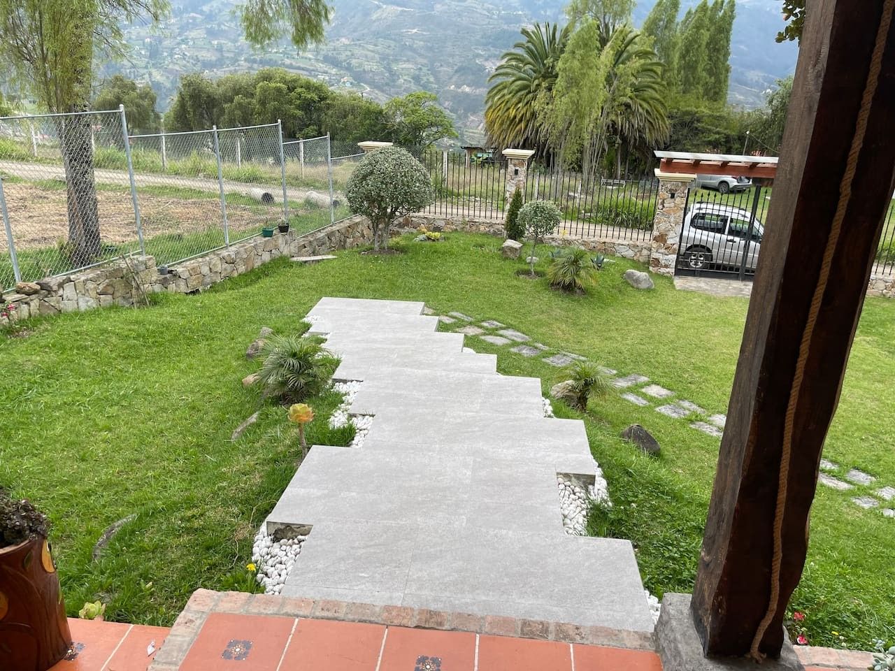 A stone pathway leading through a grassy area with a fenced property and a parked car in the background.