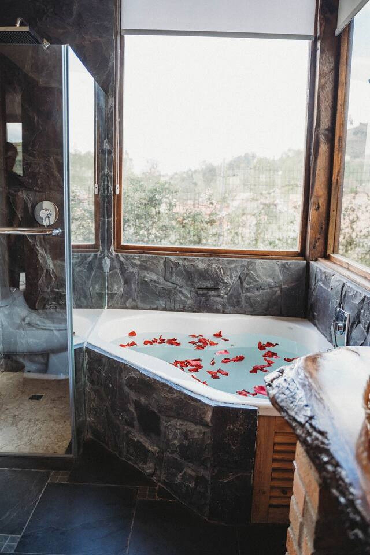 A bathroom with a stone wall, a glass shower enclosure, and a bathtub with rose petals.