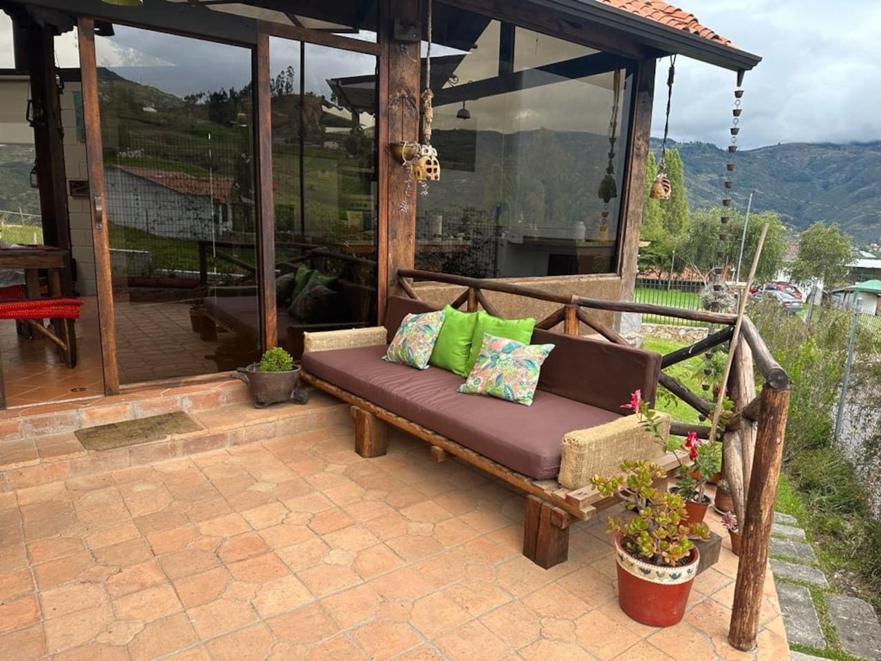 A wooden deck with a cushioned seating area, potted plants, and a view of the surrounding landscape.