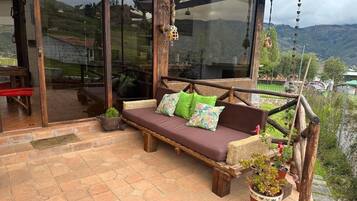 A wooden deck with a cushioned seating area, potted plants, and a view of the surrounding landscape.