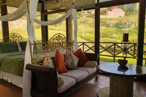A room with a bed, a sofa, and a table with a lamp. There is a view of greenery outside. - Villa Nathalie, jaccuzzi, king size bed+hammock (Chican, Paute)