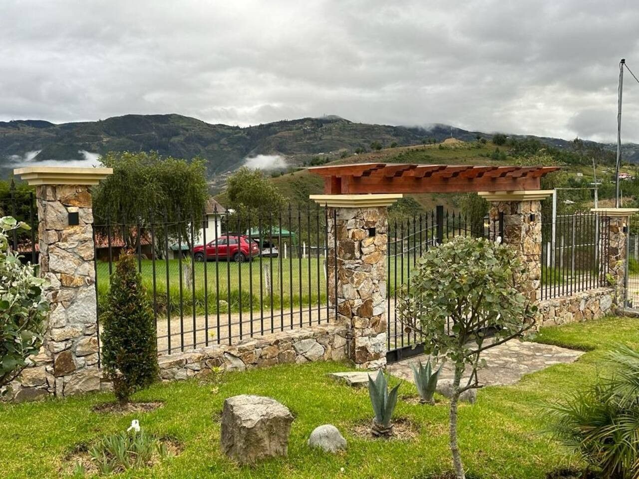 Una proprietà recintata con pilastri in pietra, un vialetto lastricato e, sullo sfondo, una macchina rossa.