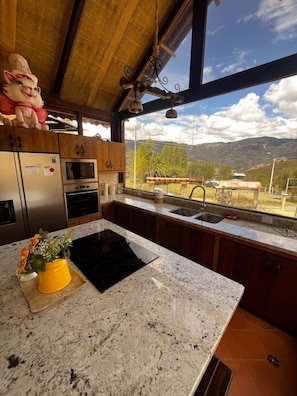Una cocina con encimeras de granito, electrodomésticos de acero inoxidable y vistas a un paisaje montañoso a través de amplios ventanales.