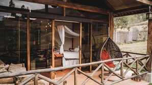 A rustic wooden structure with a glass enclosure, a bed with white bedding, and a hanging chair. - Villa Nathalie -Cheerful Rustic House (Chican, Paute)