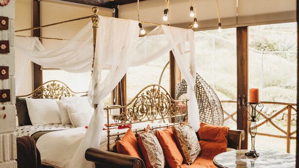 A room with a bed under a canopy, a sofa with cushions, a round table, and a view through large windows. - Villa Nathalie -Cheerful Rustic House (Chican, Paute)
