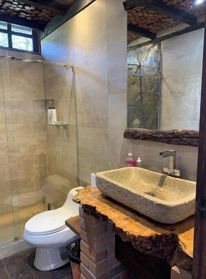 Ein Badezimmer mit einem Waschbecken aus Stein, einer Toilette und einer Duschkabine.