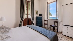 A bedroom with a bed, a dresser, two chairs, a lamp, and a window with a view. - Villino Rosa – mit Garten und Meerblick (Portoferraio)