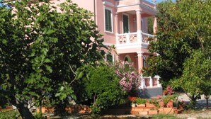 A pink villa with a balcony, surrounded by lush greenery and flowering plants. - Villino Rosa – mit Garten und Meerblick (Portoferraio)