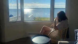 Una habitación con un ventanal grande con vistas a un cuerpo de agua, una silla de mimbre y una mesa redonda.