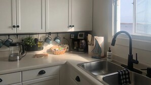 Una cocina con armarios blancos, cafetera, hervidor y lavabo.