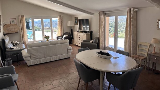 Amplia sala de estar con un sofá, mesa de comedor y sillas. Se observa un televisor y un mueble de almacenamiento al fondo.