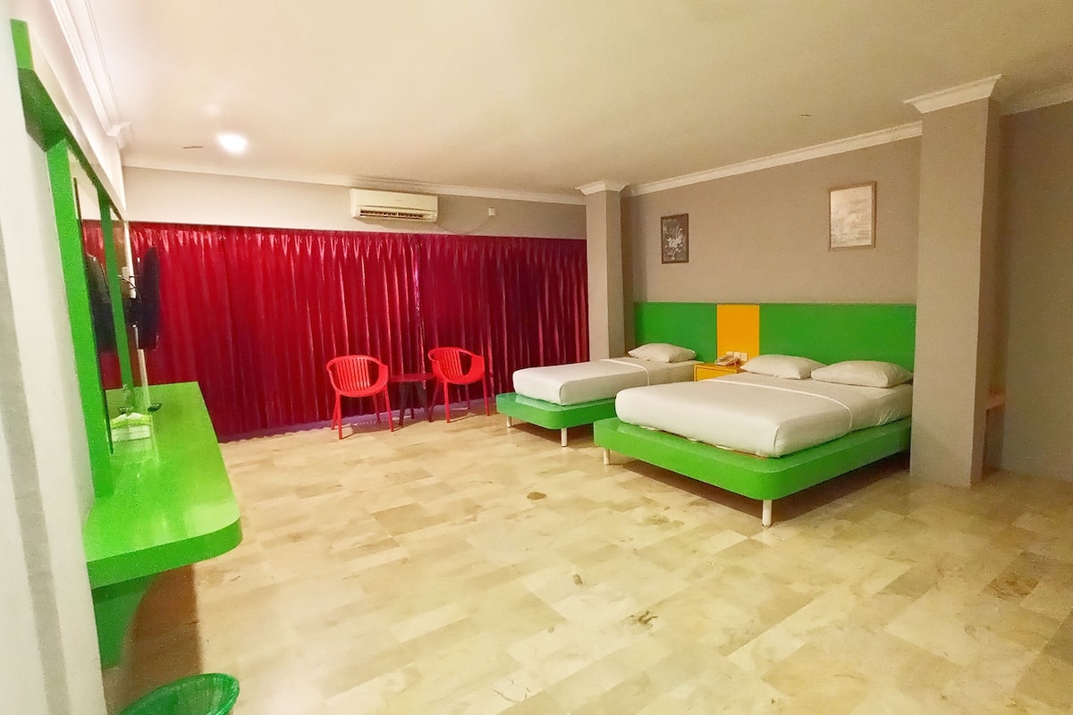 Hotellihuone, jossa on kaksi erillistä sänkyä, punainen verho, kaksi punaista tuolia ja vihreä seinä.