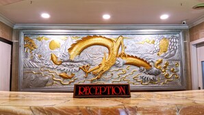 A reception area with a large decorative wall featuring a golden dragon and mountains. - Kita Hotel (Tanjung Pinang)