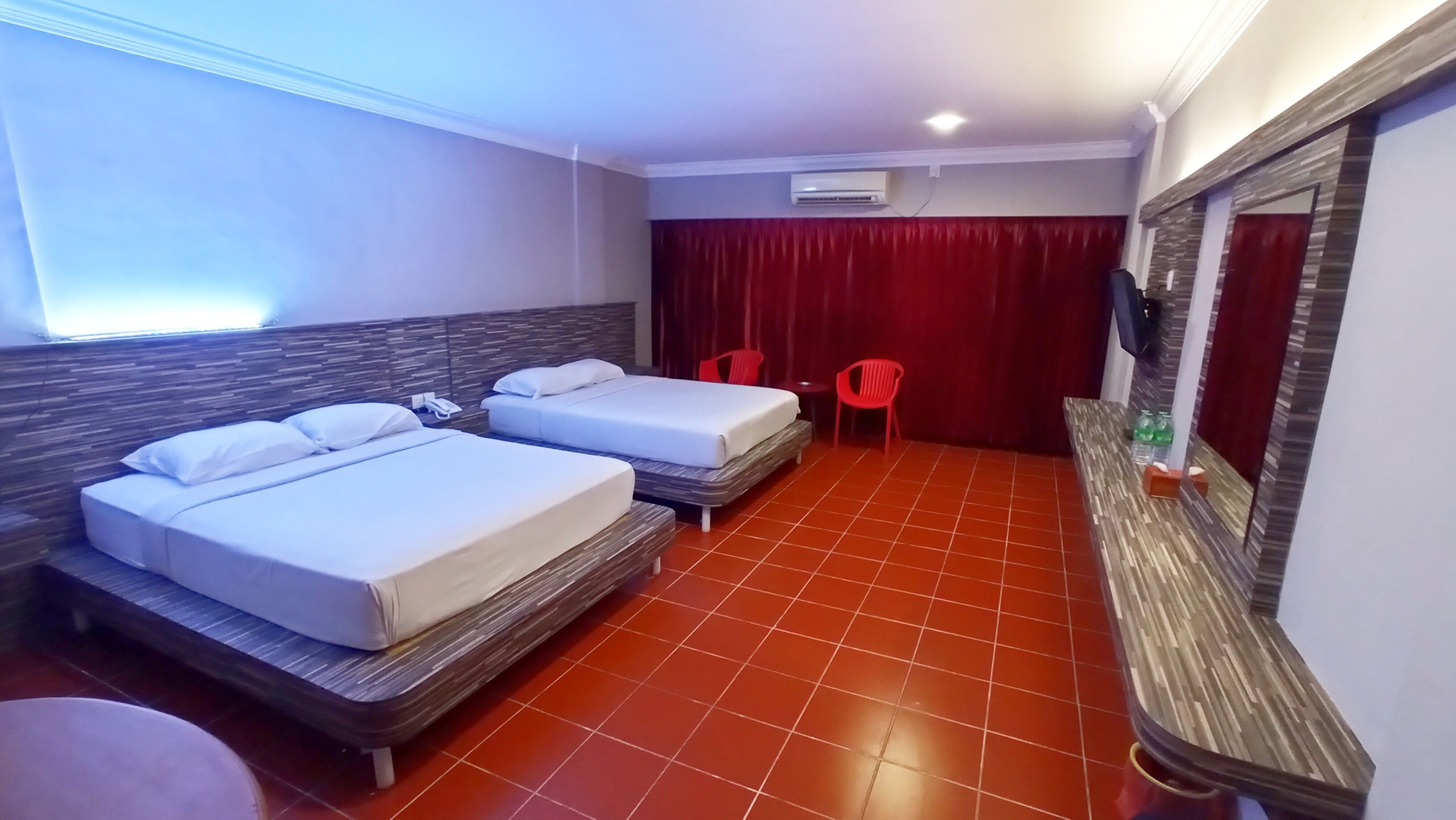 Una habitación de hotel con dos camas, televisión, cortina roja y suelo de baldosas.