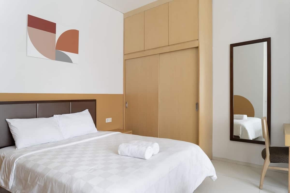 A hotel room with a bed, a wardrobe, a mirror, and a wall art piece.