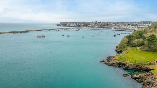 Une ville côtière dotée d’un port de plaisance, d’une côte rocheuse et d’une colline imposante, avec un sentier menant à un petit bâtiment.