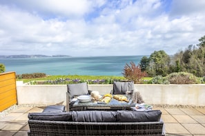Relax in a seaside seating area with a wicker sofa, glass table, and ocean views.