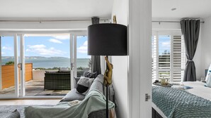 A bedroom with a large window, a bed, a bedside table, and a view of the sea. - Osprey 3, The Cove - Sea view - On site pool (Brixham)