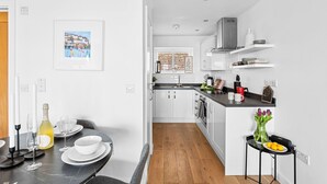 A modern kitchen with white cabinets, a black countertop, and a wooden floor. - Osprey 3, The Cove - Sea view - On site pool (Brixham)