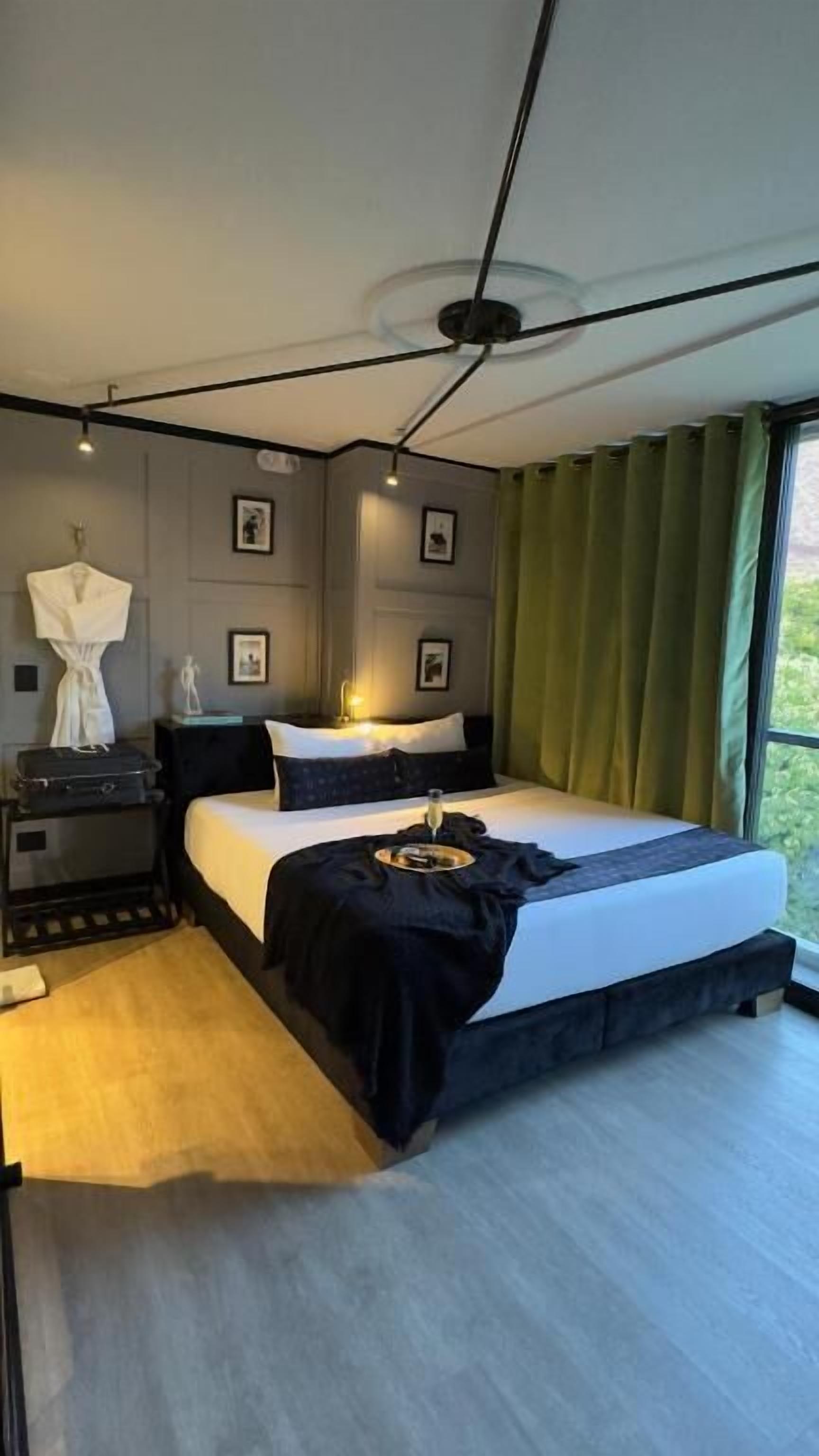 Une chambre à coucher moderne avec un grand lit, des tables de chevet, une commode et une vue sur l’extérieur.