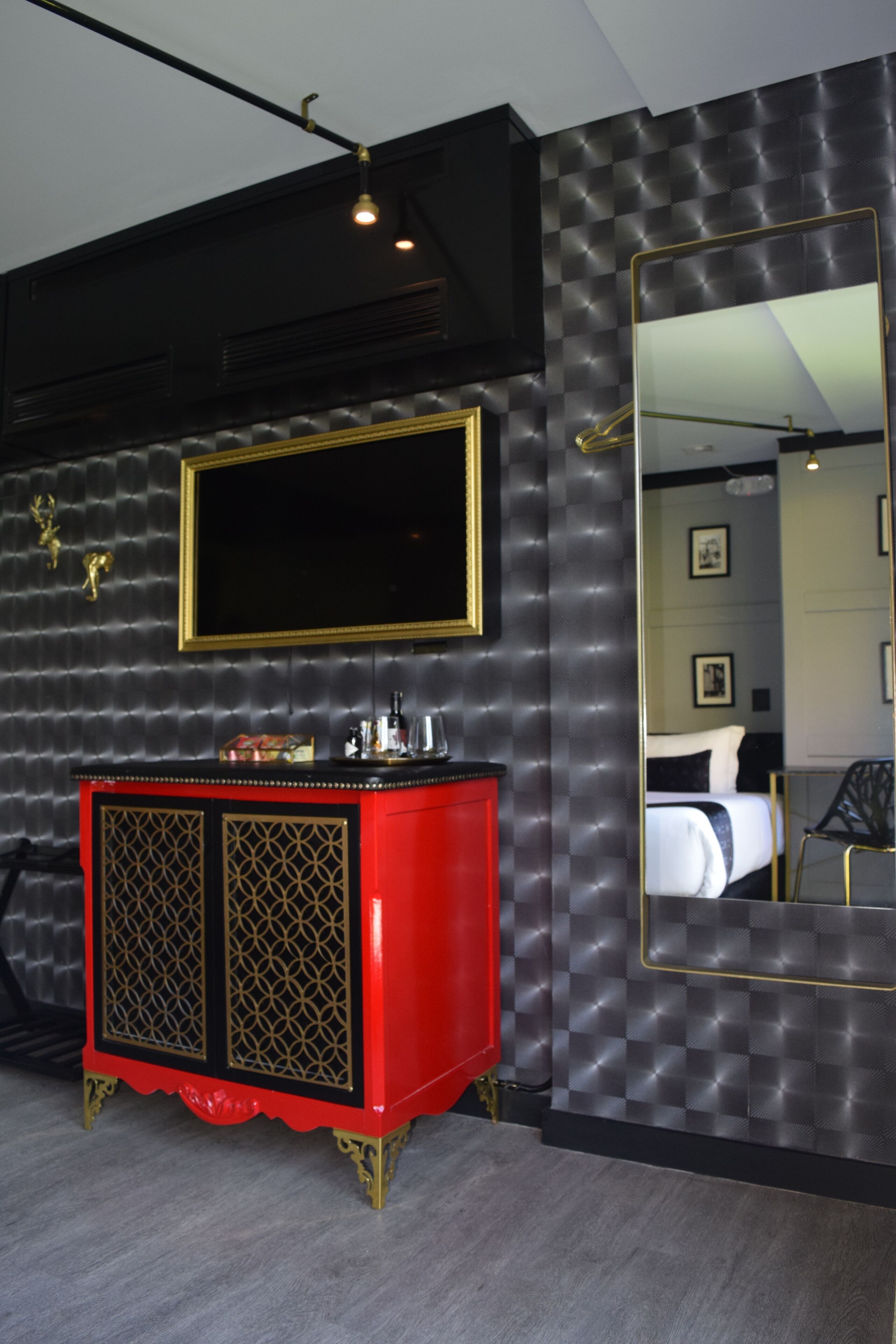 A modern hotel room with a large mirror, a red and gold cabinet, and a black textured wall.