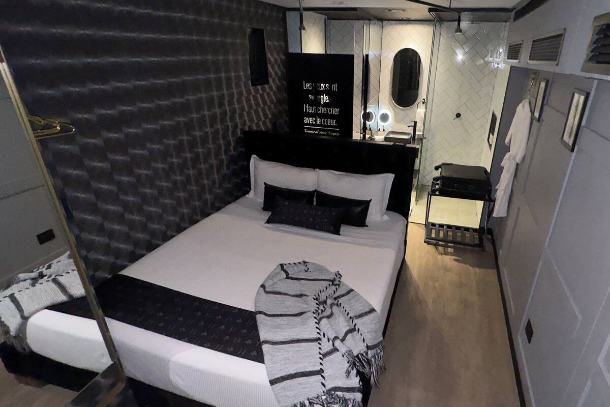 A compact bedroom with a bed, a vanity with mirrors, and a small seating area.