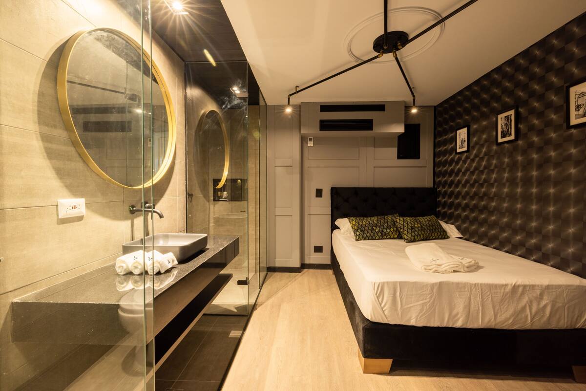 A modern hotel room with a large bed, a round mirror, a sink, and a dark patterned wall.