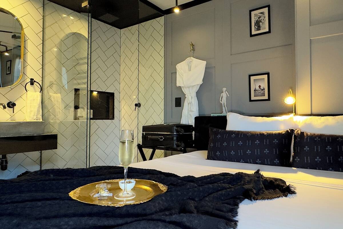 A modern hotel room with a bed, a bedside table, a mirror, a dresser, and a wall with framed pictures.