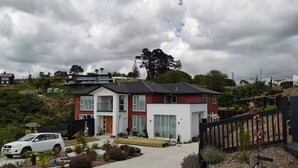 A two-story house with a balcony, surrounded by landscaped gardens and a car parked in the driveway. - Penelope garden ,5 min to Botany shopping mall (Auckland)