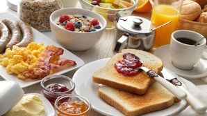 A breakfast table with various foods including scrambled eggs, sausages, toast with jam, cereal, fruit, and orange juice.