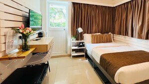 A hotel room with a bed, a desk with a computer, a TV, and a window with curtains.