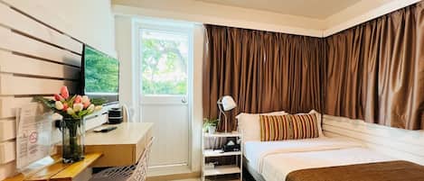 A hotel room with a bed, a desk with a computer, a TV, and a window with curtains.