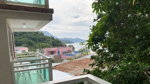 A balcony with a glass railing overlooking a swimming pool and a view of buildings and mountains.