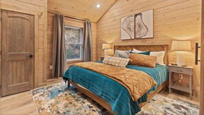 Ein Schlafzimmer mit Holzwänden, einem Bett, Nachttischlampen und einem Fenster mit Vorhängen.
