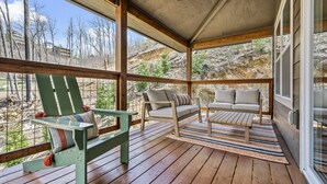 Ein überdachter Außenbereich mit Holzterrasse, einem grünen Adirondack-Sessel, einer Couch und einem kleinen Tisch.