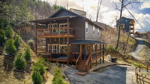Una casa di legno a due piani con un balcone, immersa tra gli alberi e affiancata da un sentiero sterrato.